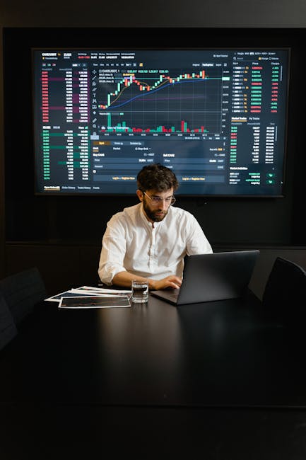 About A focused man analyzing stock market trends on a laptop in an office setting with charts displayed.